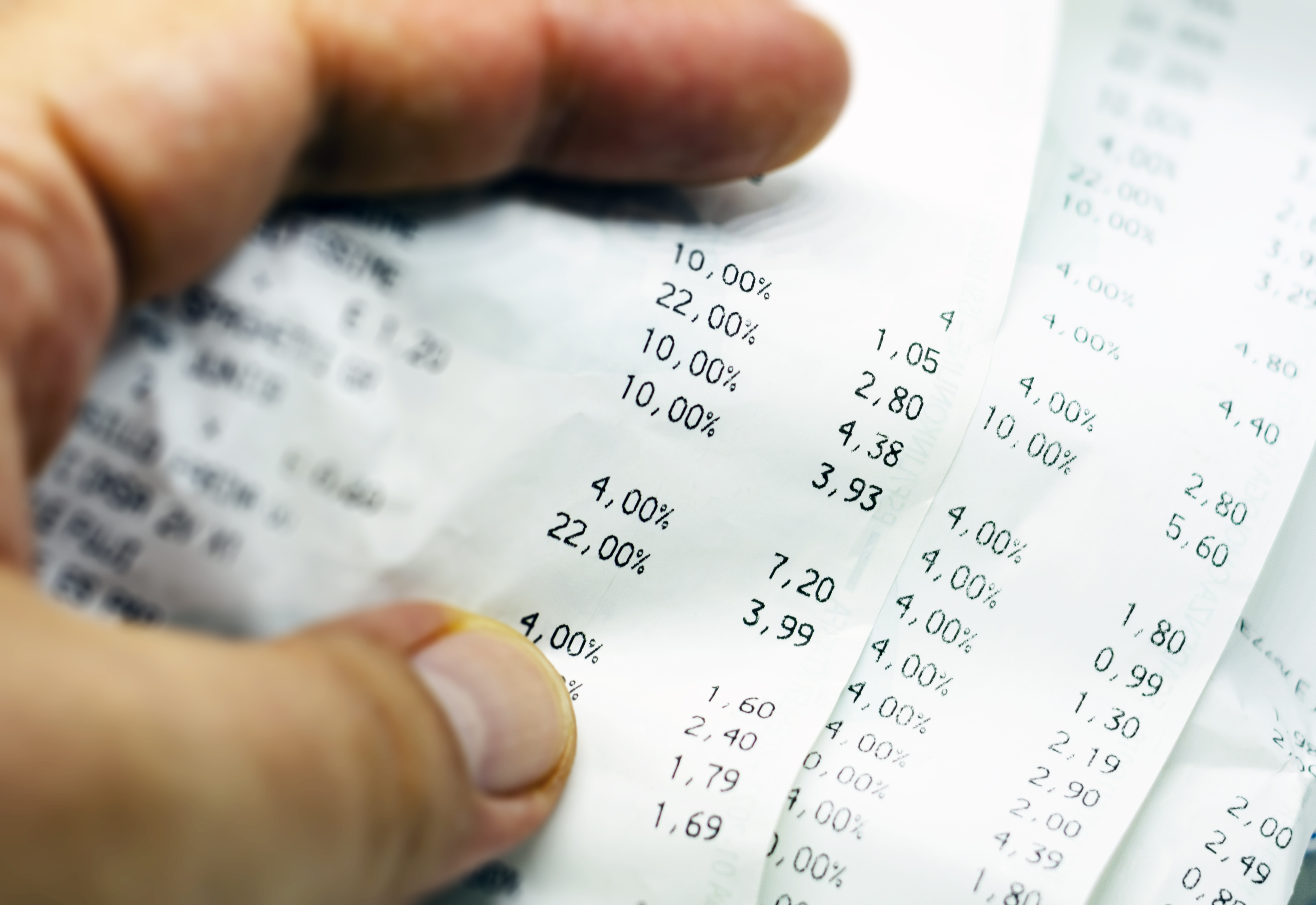 人の指がレシートを持っていて、割引や価格などの数字が印刷されています。