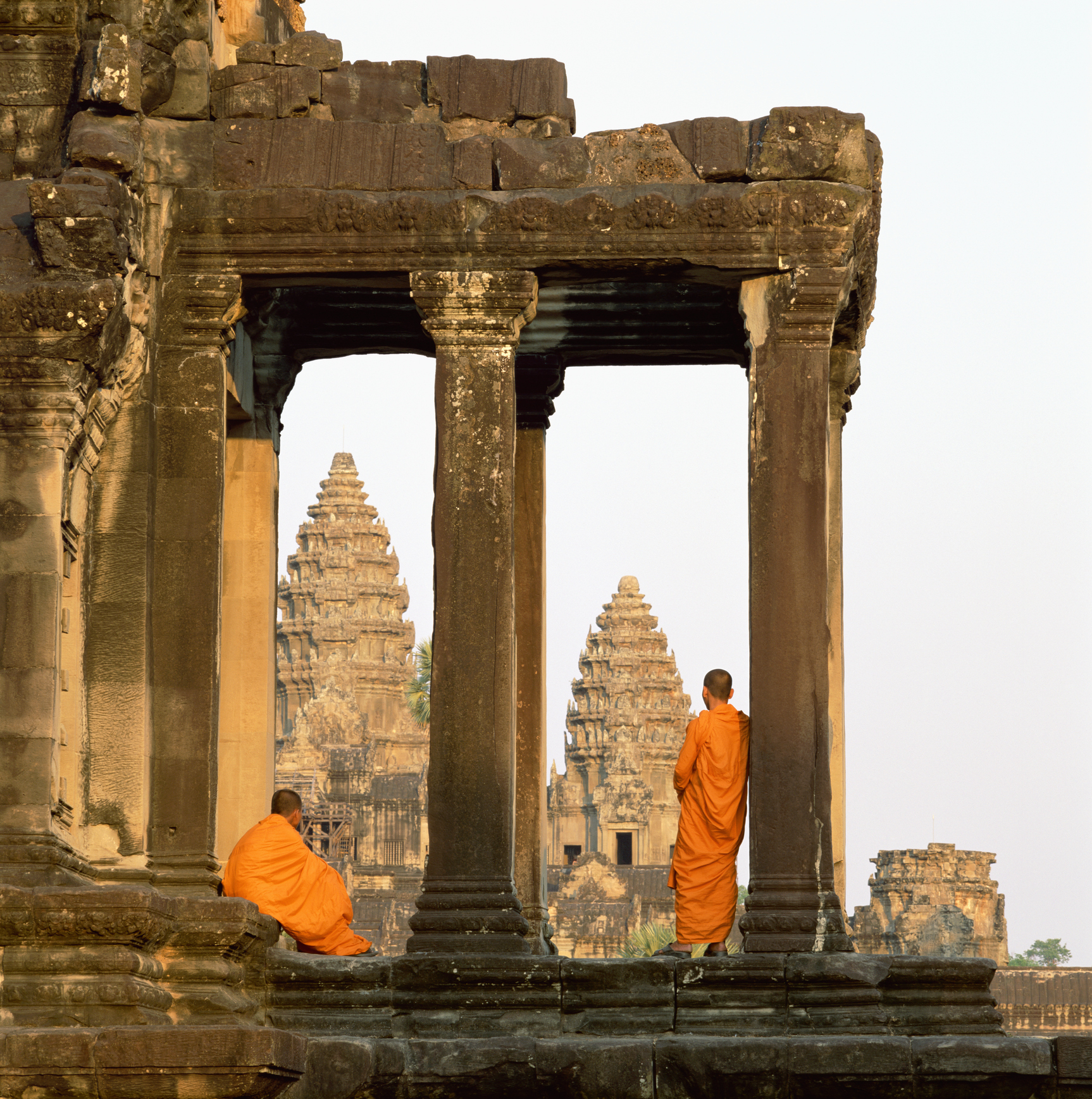 Two monks stand by a temple&#x27;s ancient ruins, looking toward central towers