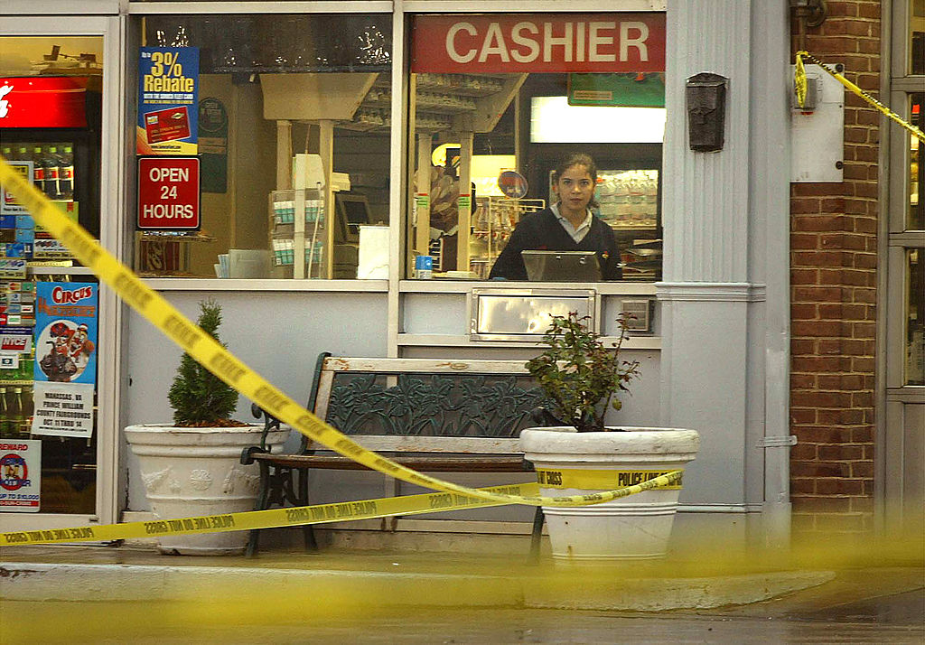 A cashier stands behind a convenience store counter with police tape in the foreground