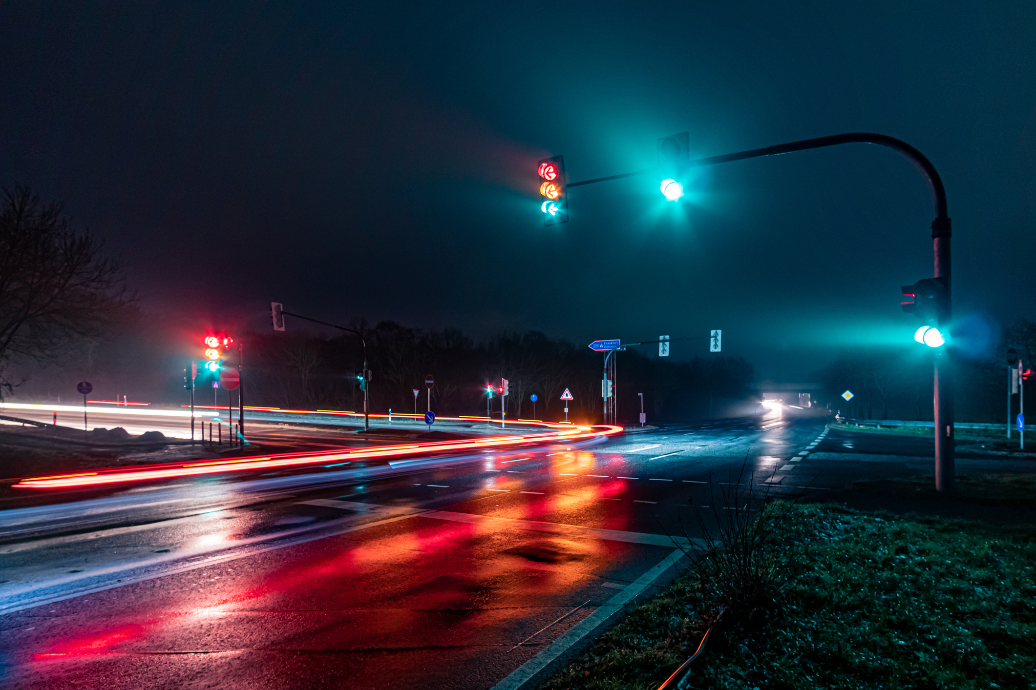 Traffic lights on a misty night with car light trails and reflections on the wet road