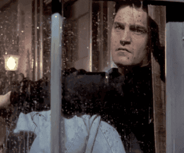 Chandler Bing gazes out a window with a reflective expression as rain pours down outside