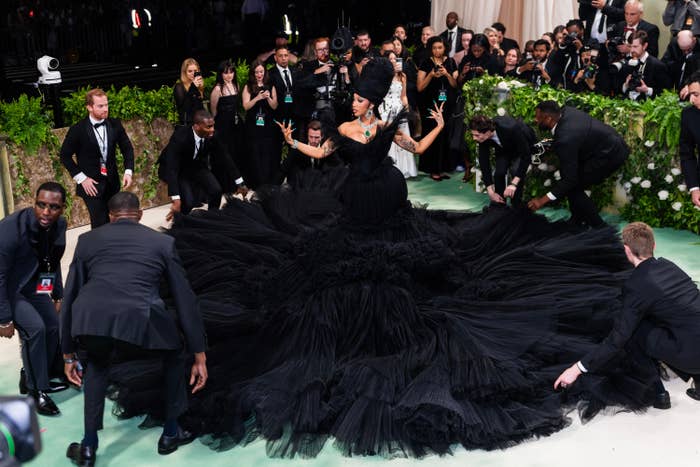 Cardi B on Met Gala stairs in voluminous black gown with assistants adjusting the train