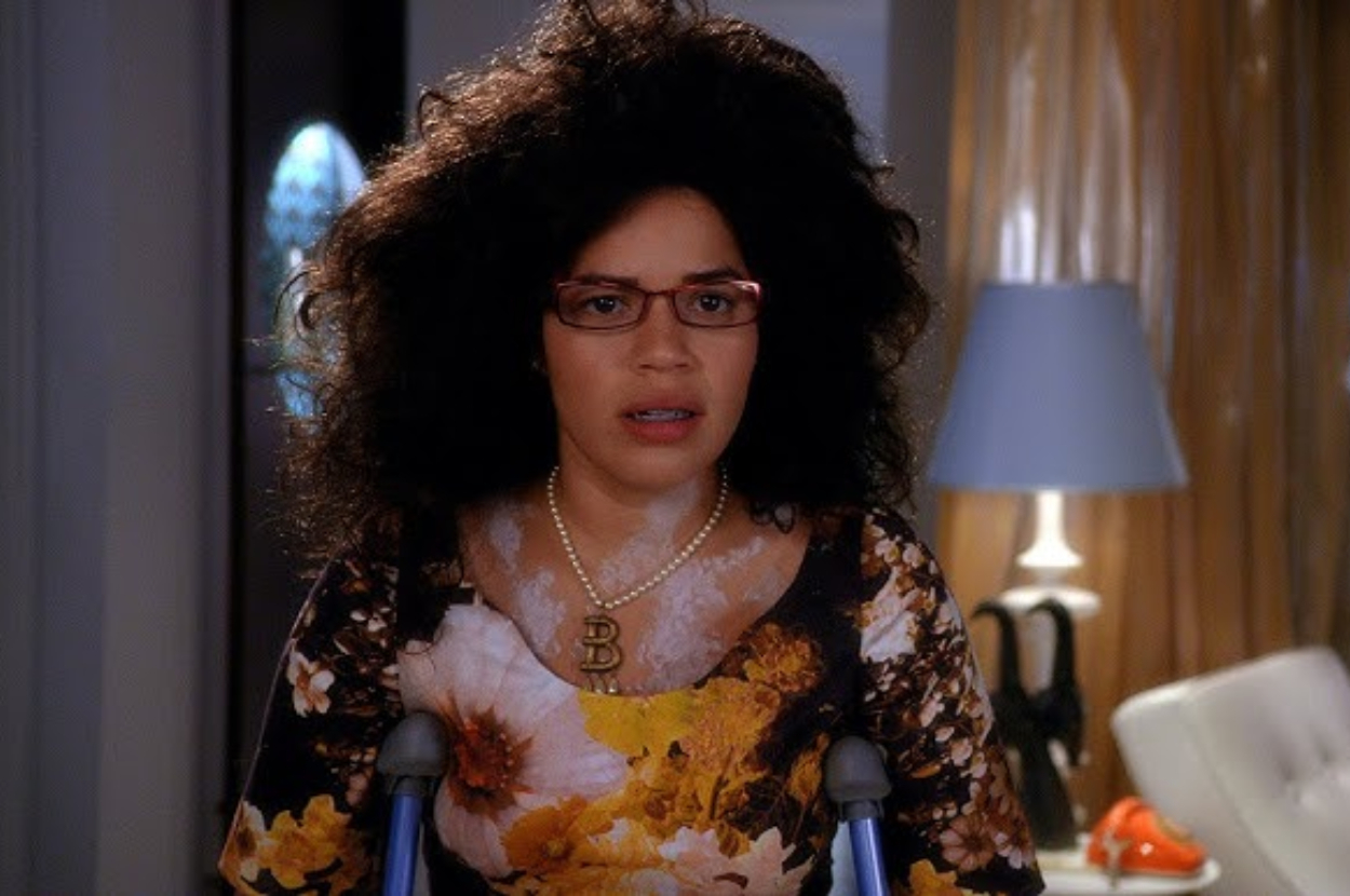 Betty Suarez from Ugly Betty in a floral blouse, with a large, frizzy hairstyle, and glasses, looking surprised