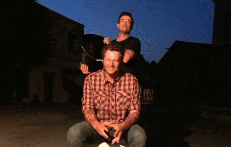 Two men are participating in the ALS Ice Bucket Challenge, one standing and pouring a bucket onto the other who is seated
