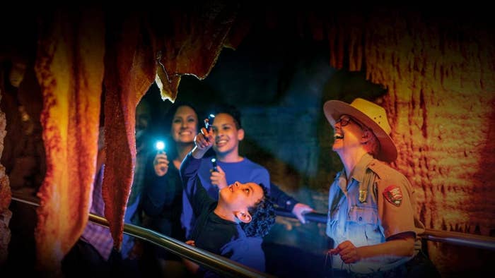 A park ranger guides visitors on a cave tour, shining a light on the formations as the group looks on with interest
