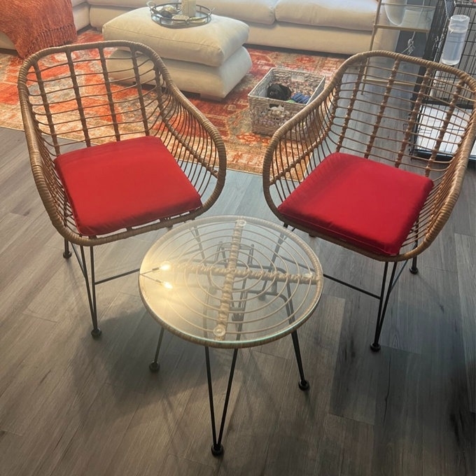 Two wicker chairs with red cushions and a small round glass table, indoors