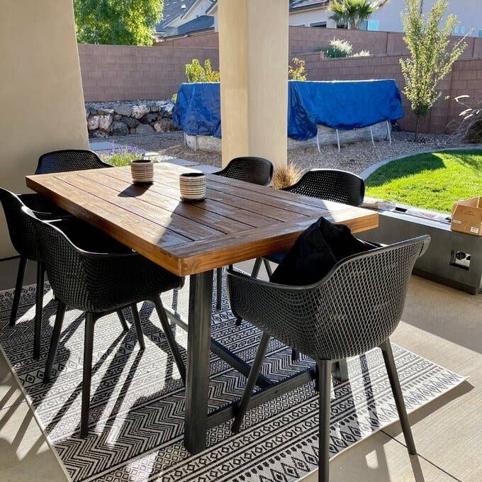 Outdoor dining area with a wooden table, black chairs, and geometric rug. Suitable for patio design ideas