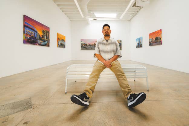 Man seated on a bench in an art gallery showcasing paintings, focusing on his sneakers