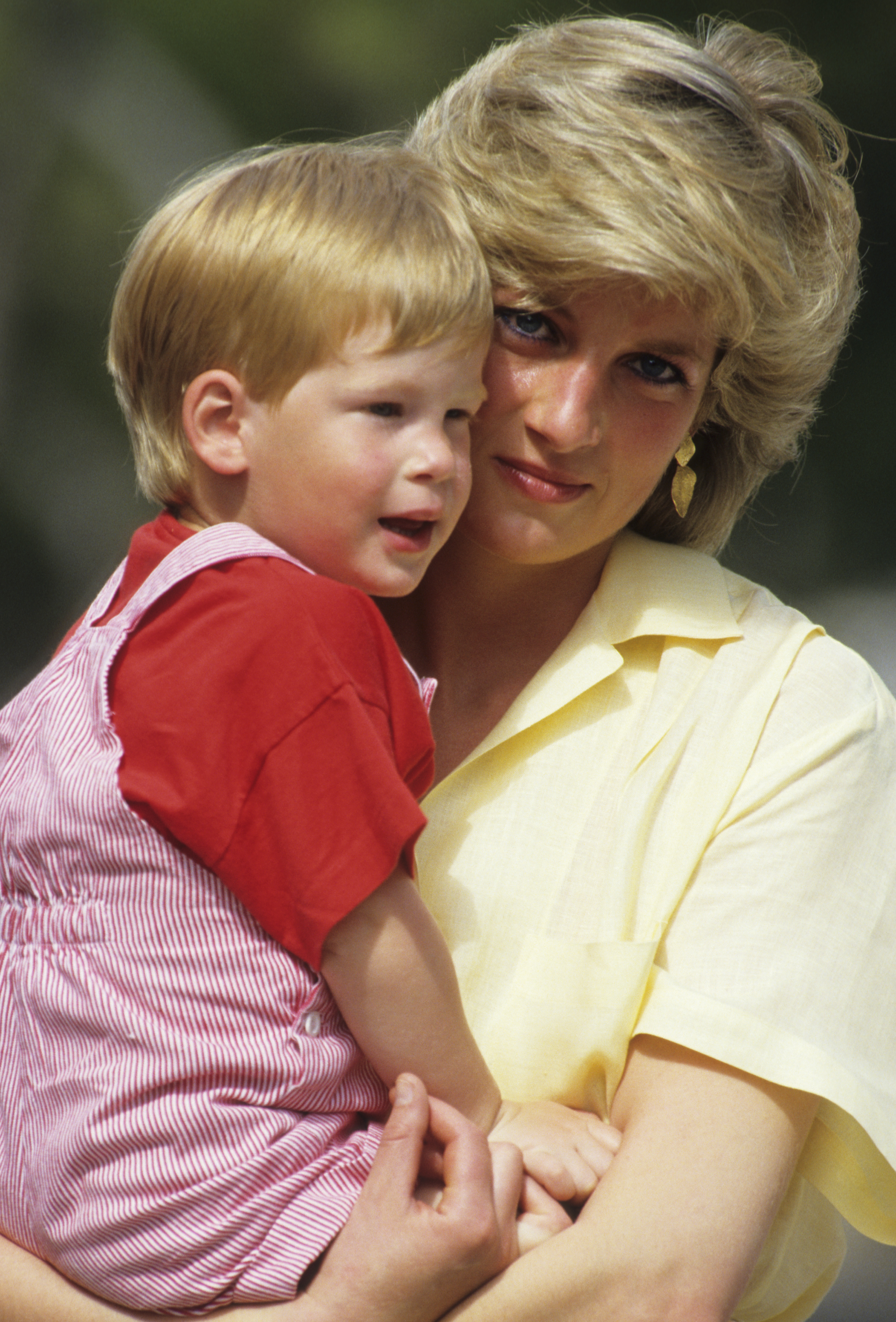 Princess Diana holds a young Prince Harry, both smiling in casual attire