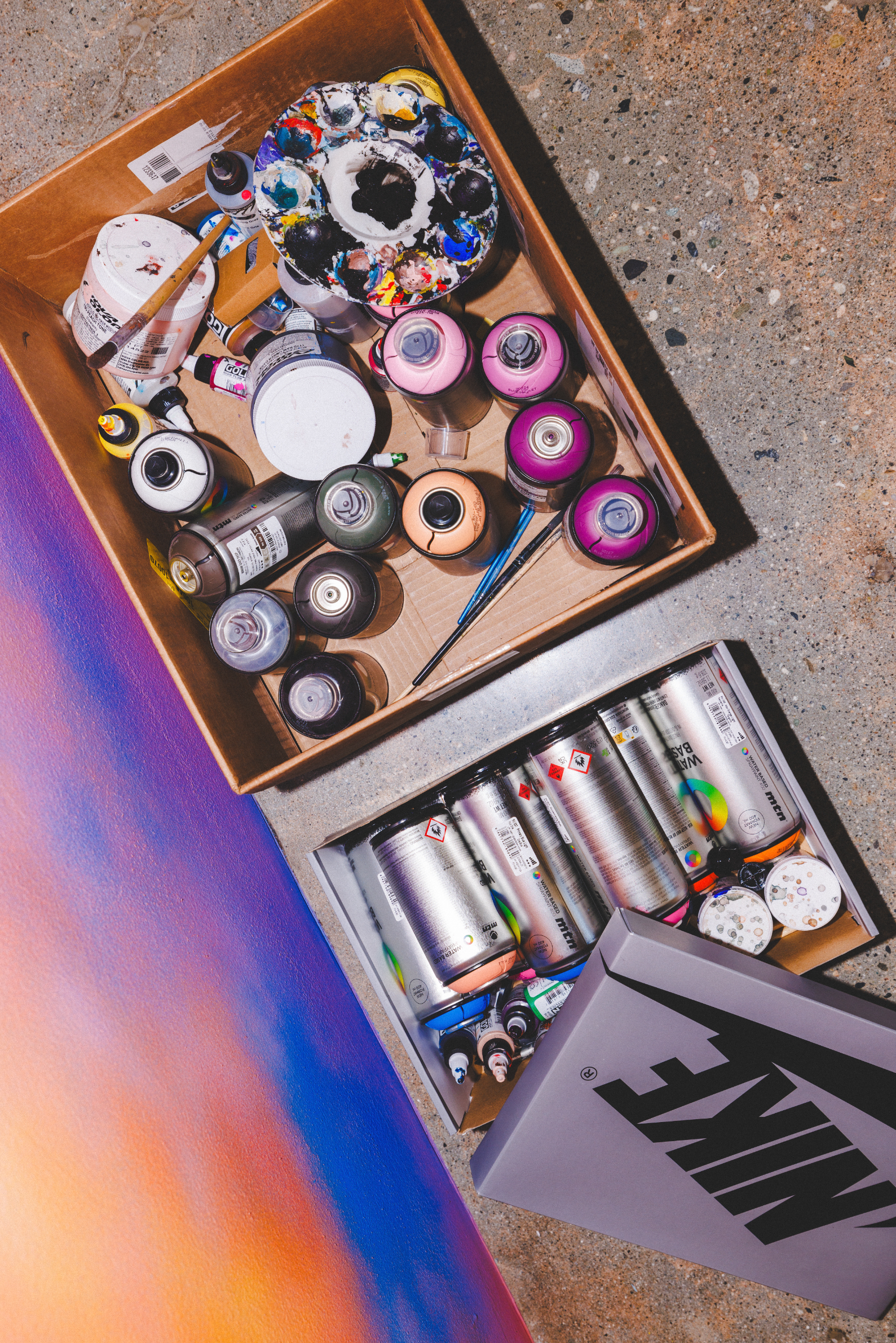 A box of various spray paint cans next to a painted sneaker and graffiti artwork