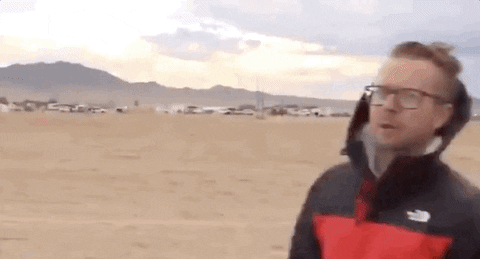 Reporter holding a microphone with a "THE BIG STORY" banner, looking surprised as wind tousles hair