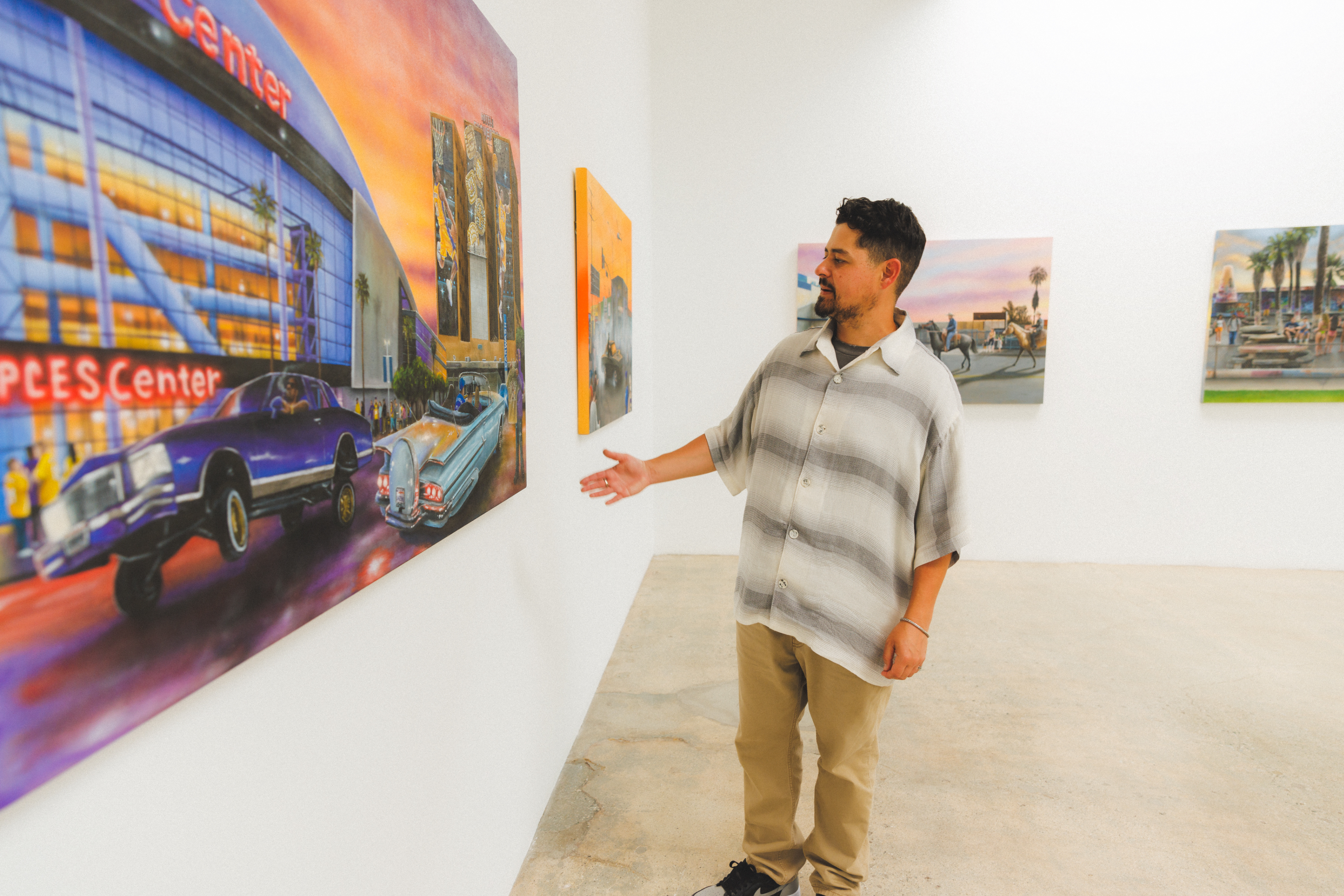 Man in a plaid shirt at an art gallery points at a painting, wearing casual sneakers