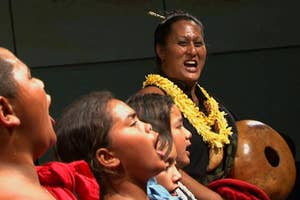 Three individuals performing a traditional chant, the central person wearing a lei