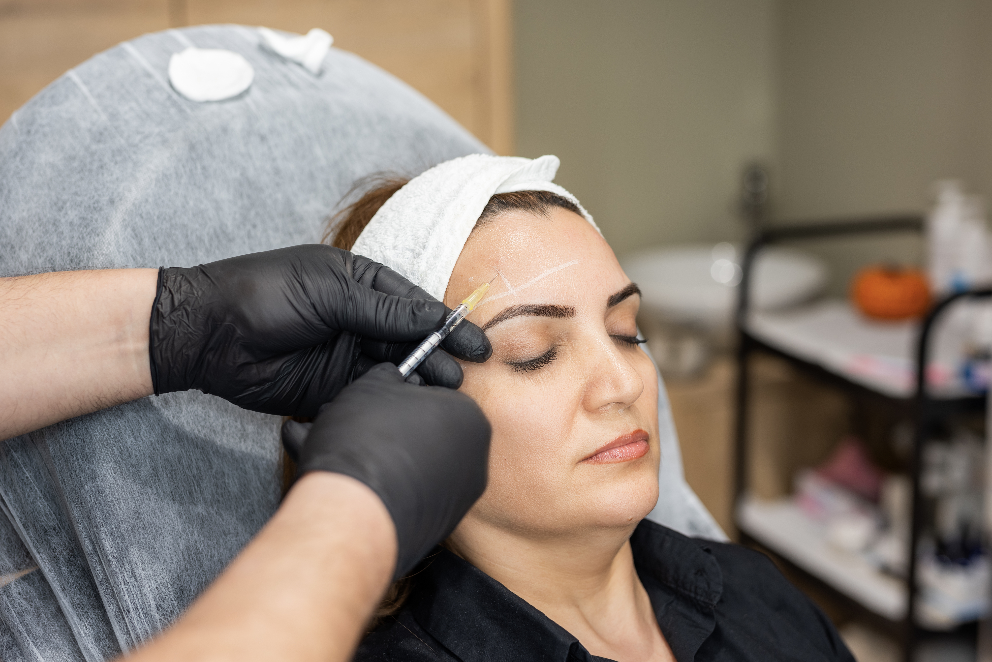 A person receiving eyebrow microblading treatment from a technician in a salon setting