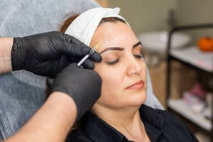 A person receiving a cosmetic eyebrow treatment with a tool