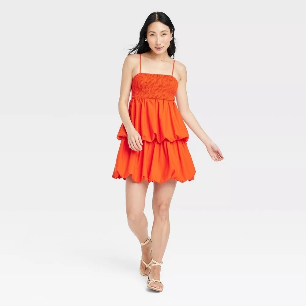 A model wearing a strapless orange bubble mini dress and white strappy heels