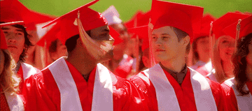 Graduados en togas rojas y birretes animan durante una ceremonia al aire libre