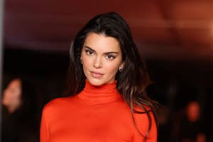 Kendall Jenner standing, wearing a fitted red turtleneck top at an event