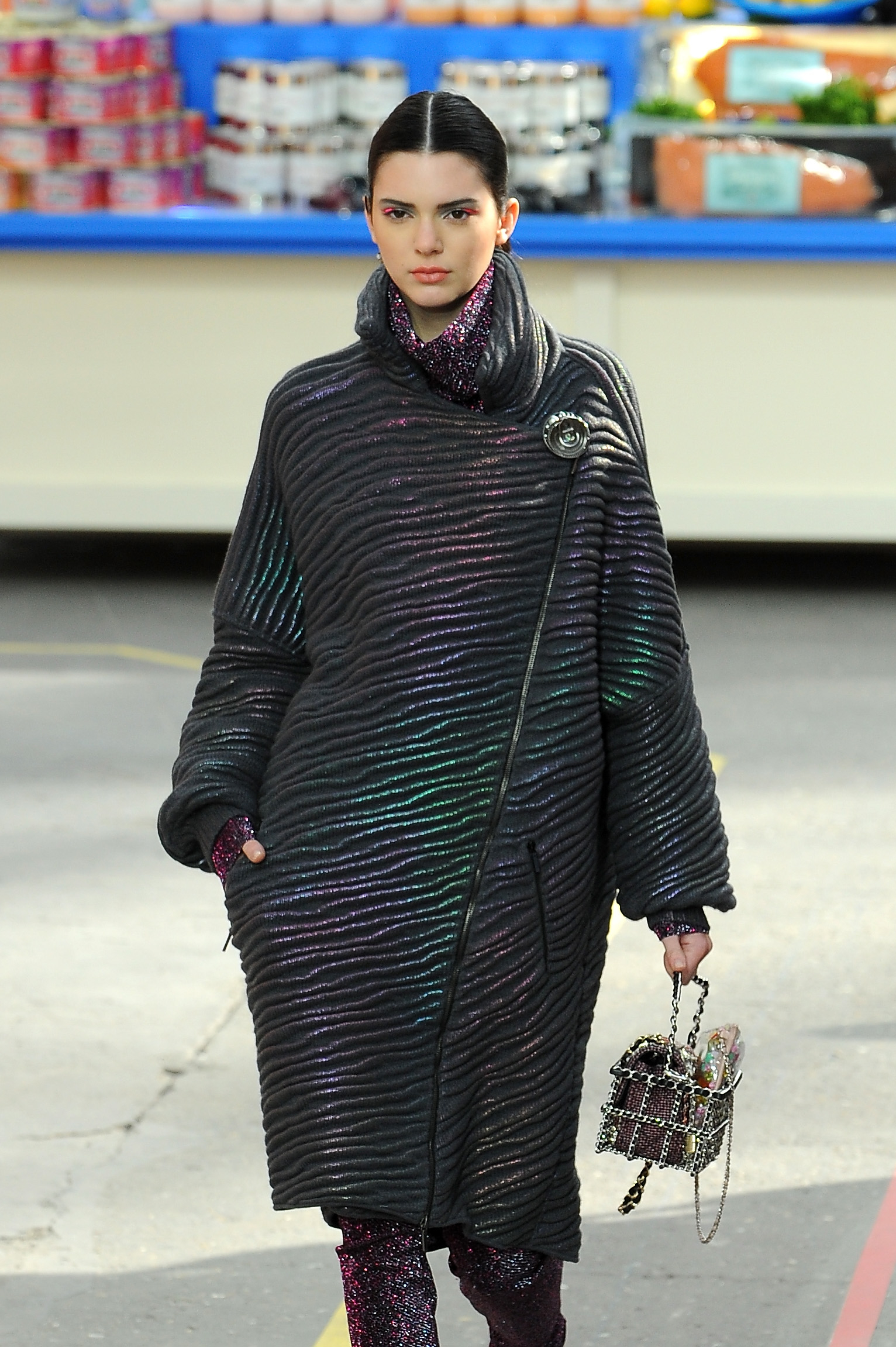 Kendall Jenner on runway in a sparkling oversized coat with metallic finish and matching leggings, accessorized with a small bag