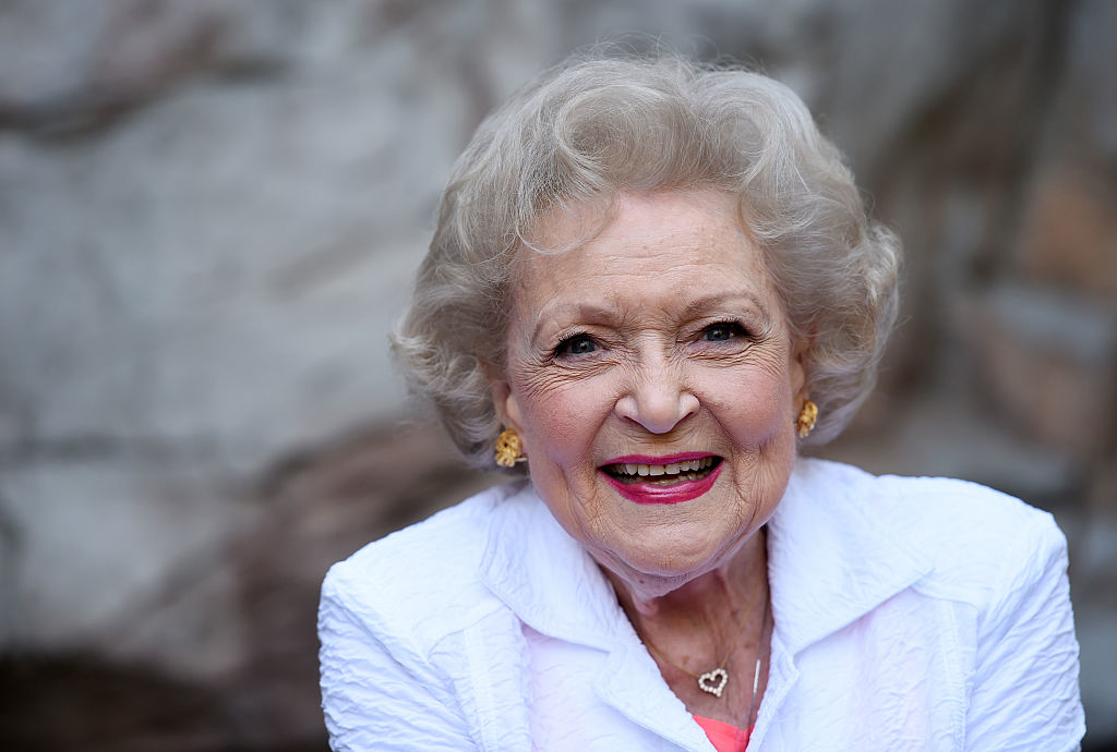 Betty White smiling for the camera, wearing a white top and gold earrings