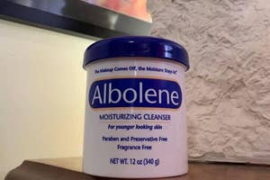Albolene moisturizing cleanser jar on a shelf, labeled for younger-looking skin, preservative-free