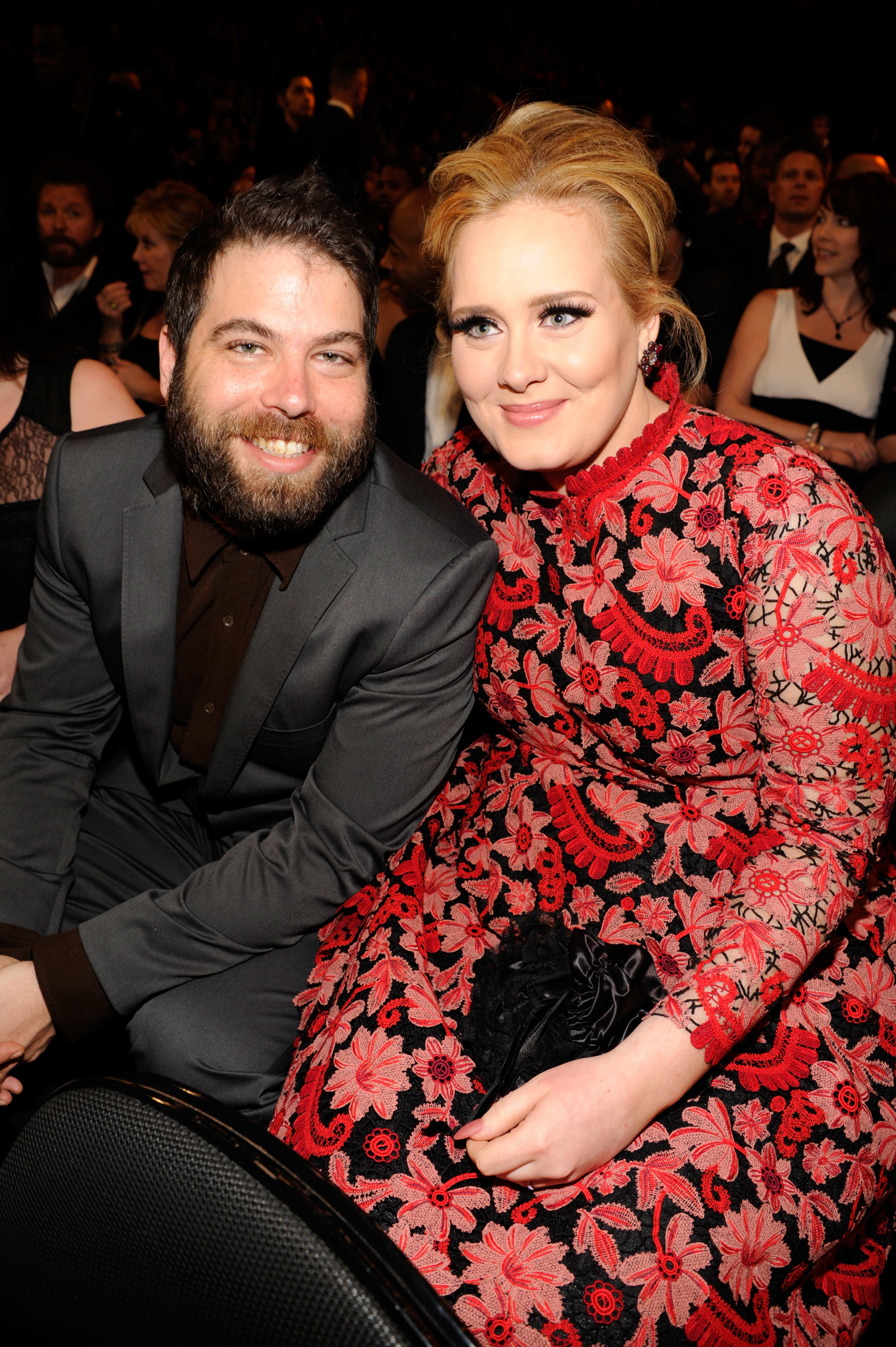 Two people seated at an event, one wearing a floral-patterned dress, the other in a suit