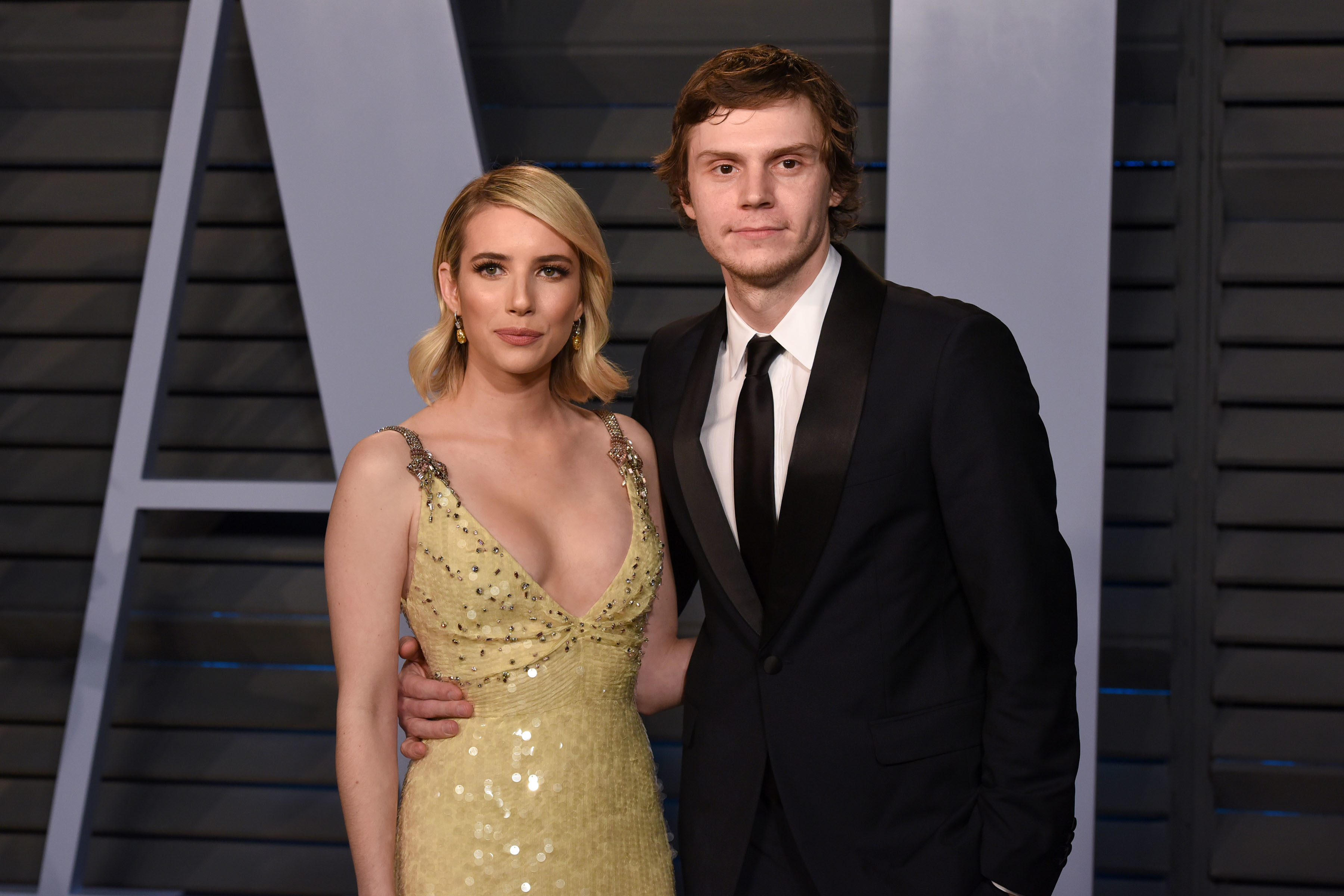 Two people posing, one in a sequined gown and the other in a suit and tie, at an event