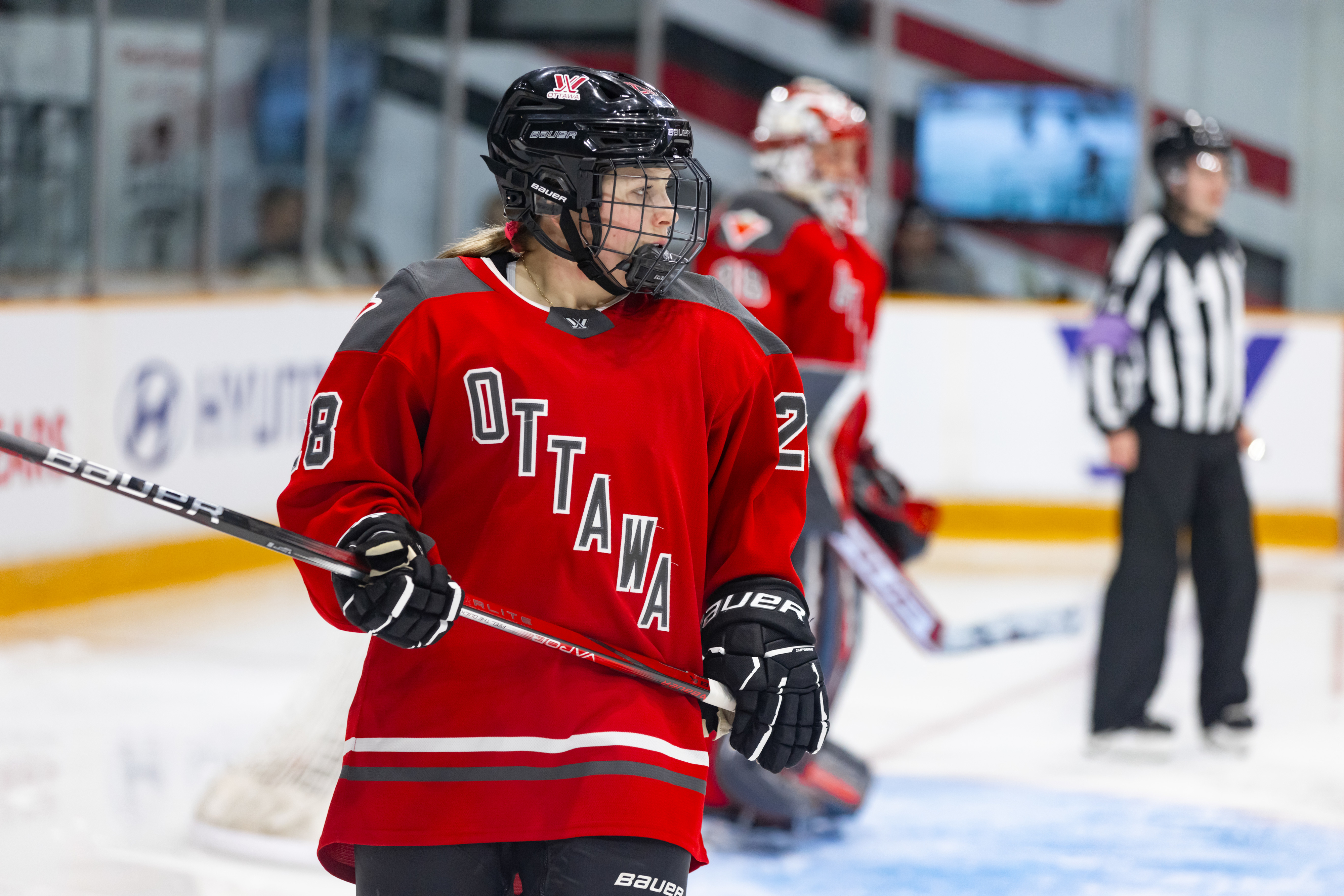 Hockey player in Ottawa jersey on ice rink with teammates and referee in background