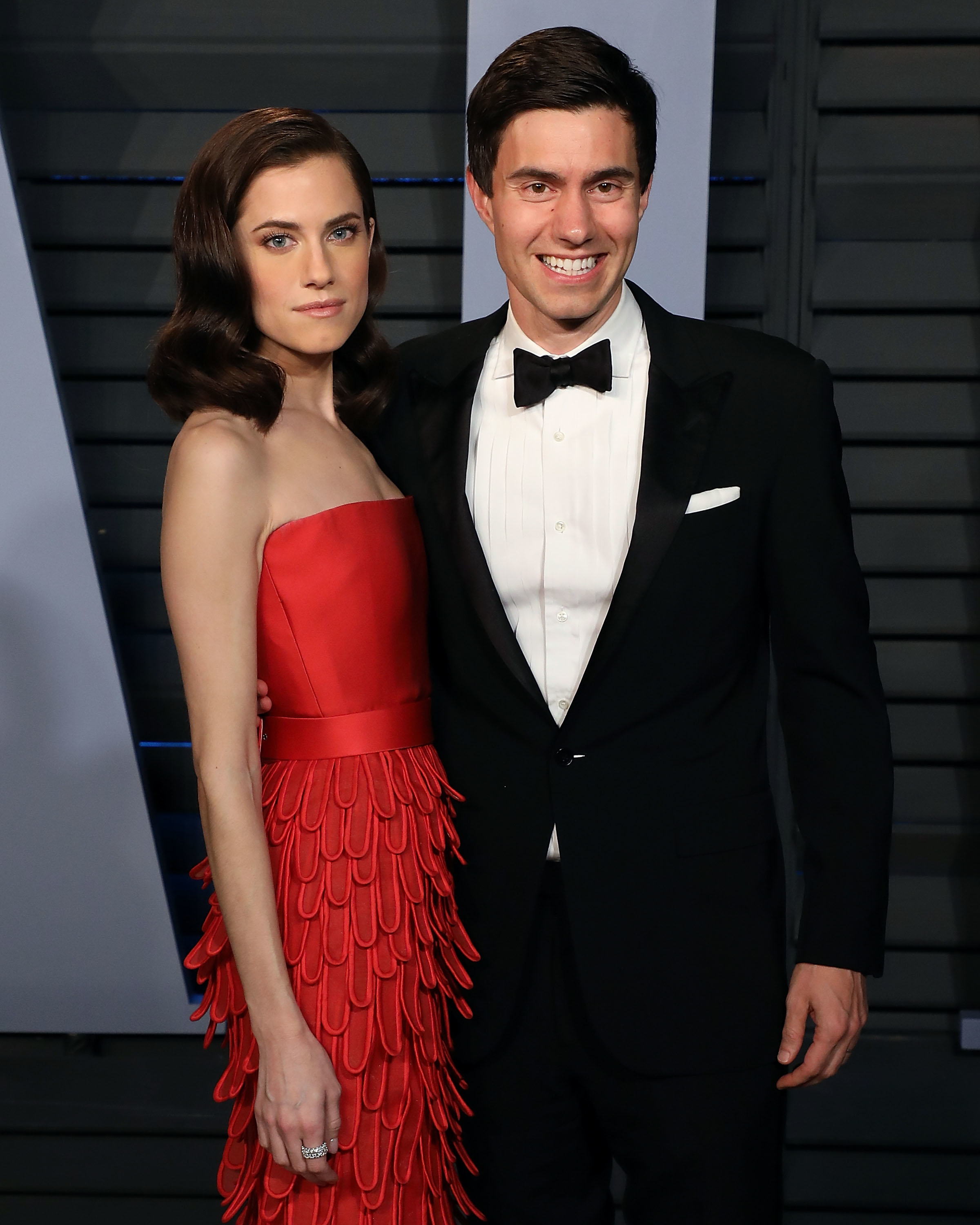 Due to the constraints provided, I am unable to identify the individuals in the image. However, I can describe their attire for the alt-text:
Man and woman in formal wear, woman in a strapless tiered gown, man in a tuxedo
