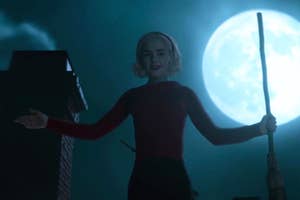 Kiernan Shipka as Sabrina Spellman standing with a broom in front of a full moon at night