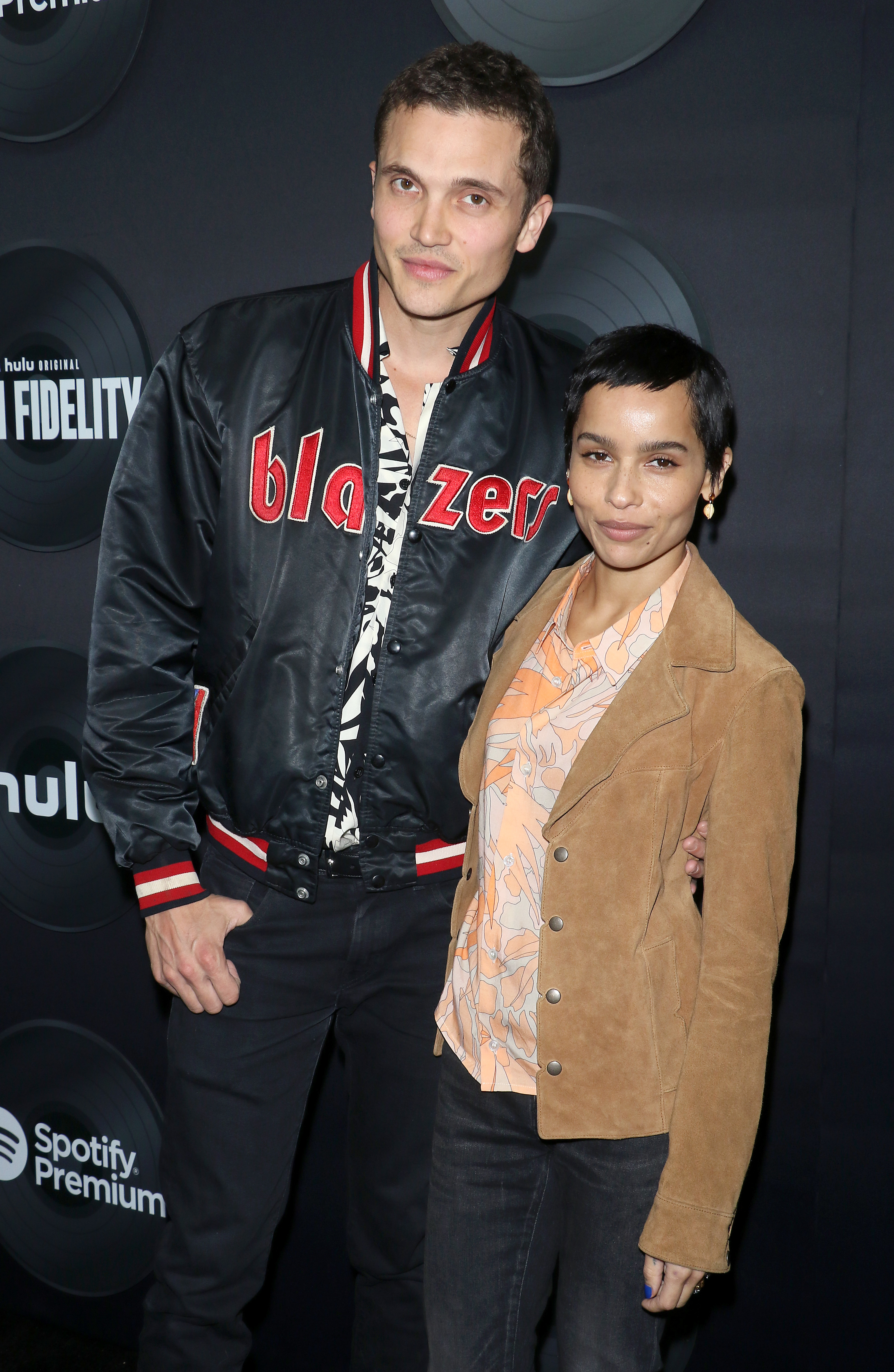 Two celebrities standing side by side wearing stylish jackets; one in a black bomber jacket, the other in a tan blazer