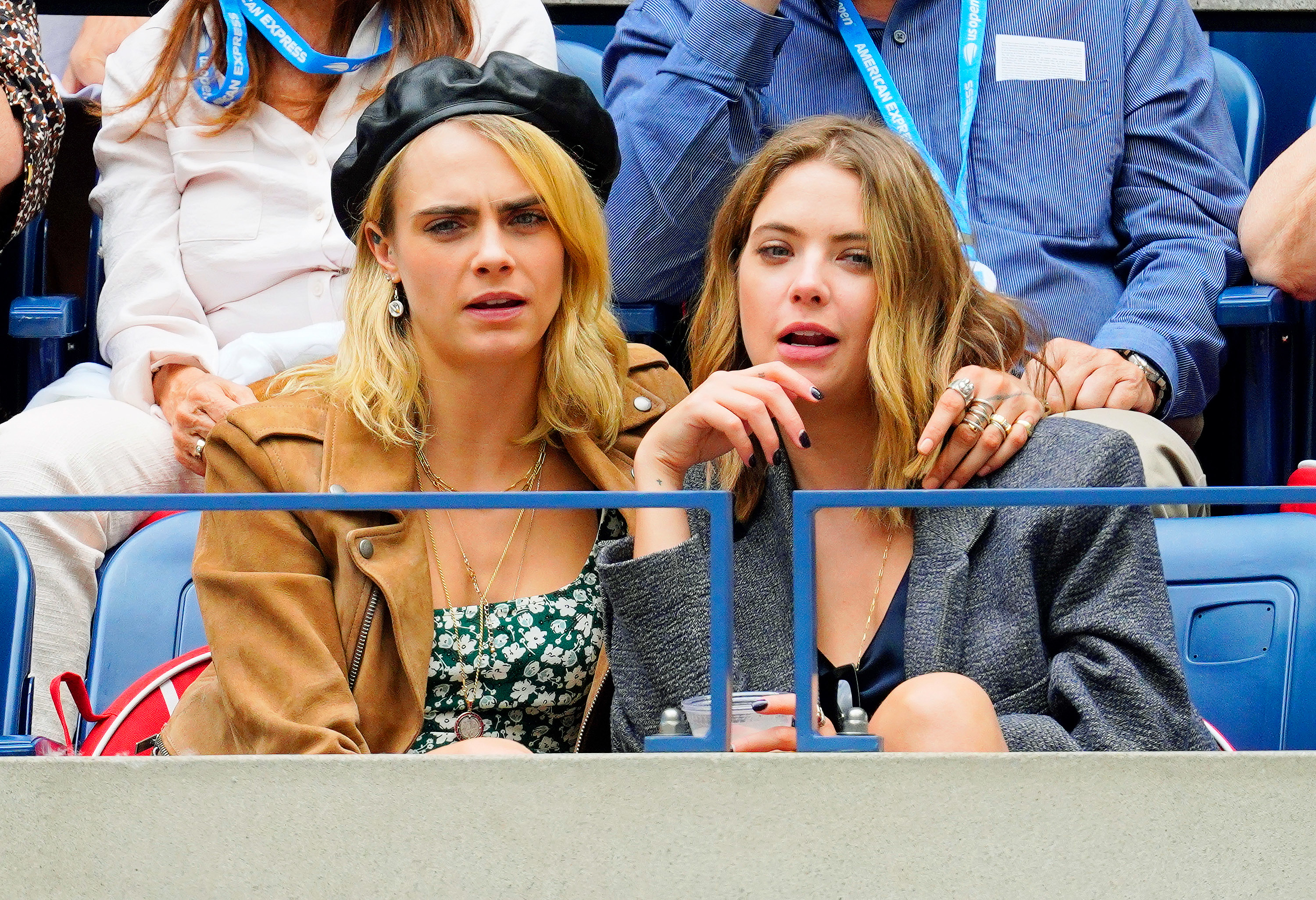 Two women in casual attire sitting and watching an event, showing surprised facial expressions