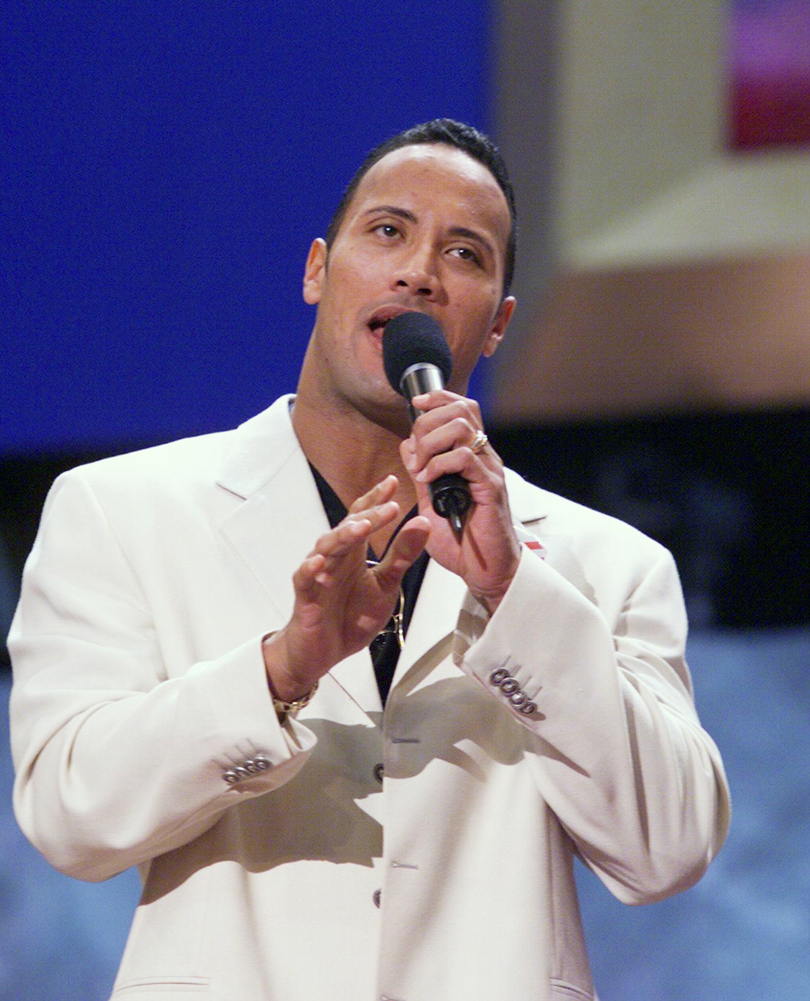 Man in white suit performing on stage with a microphone