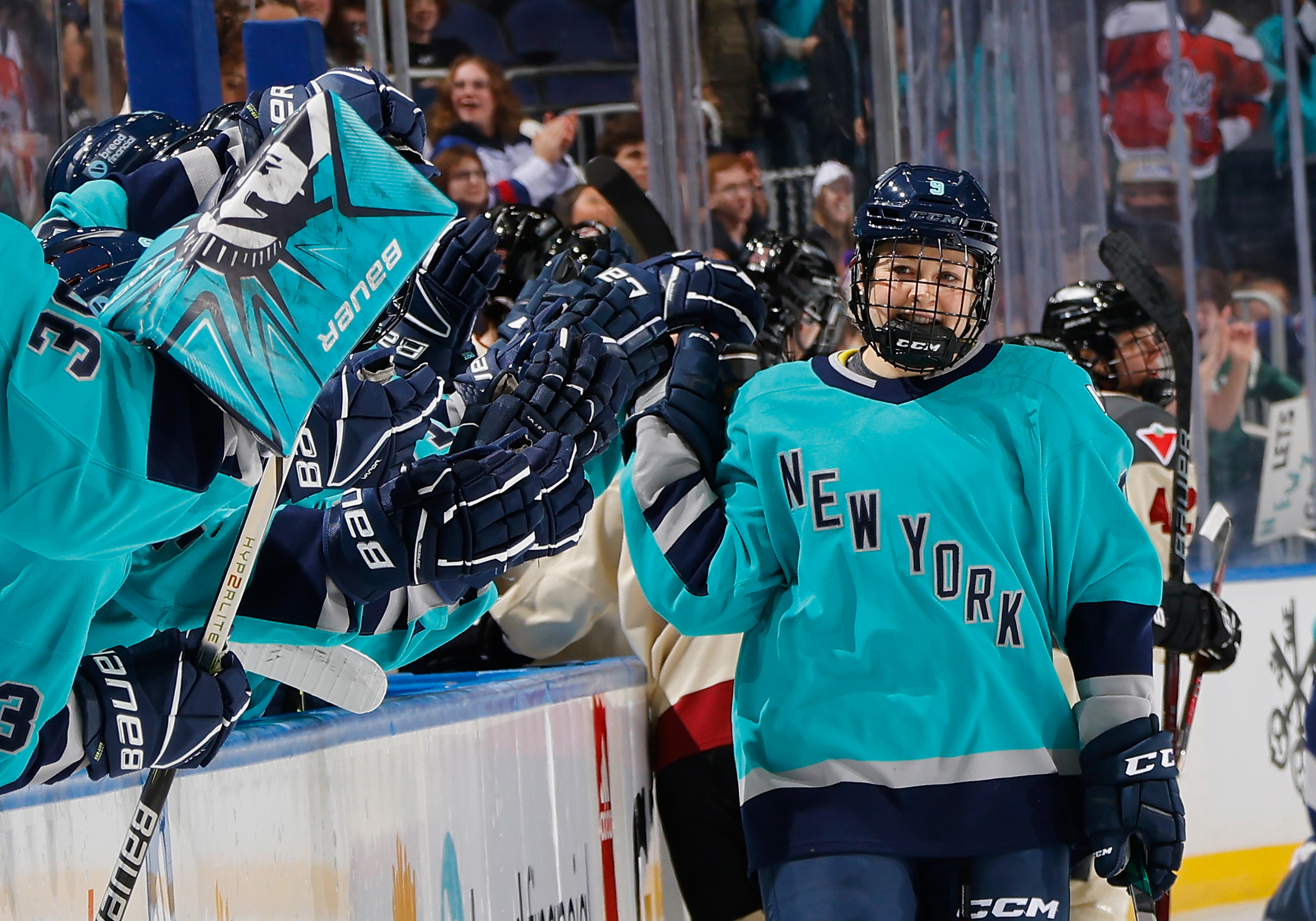 Ice hockey players in action on the rink, wearing "New York" jerseys, with gear and fans in background