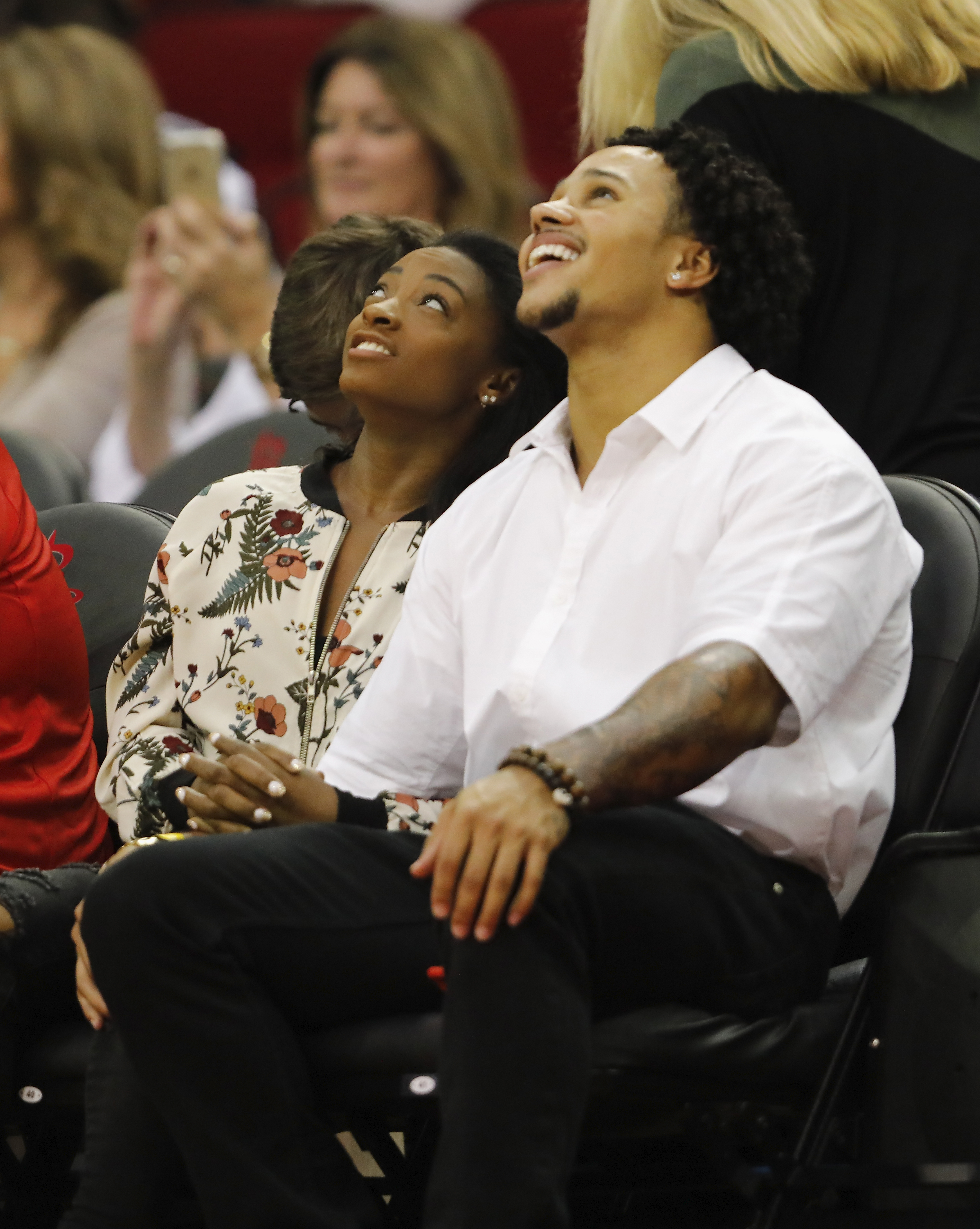 Two people seated at a sports event, looking up with engaged expressions, the person on the right wearing a white shirt