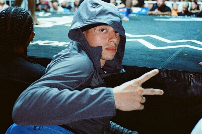 Person in hooded attire poses with a peace sign at a music event