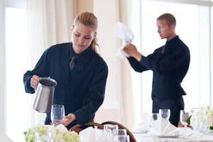 Server in uniform pouring water at a dining table, another staff member in background