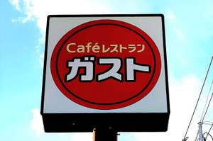 Sign for "Café de Kureyon" against the sky, with Japanese script inside a red circle