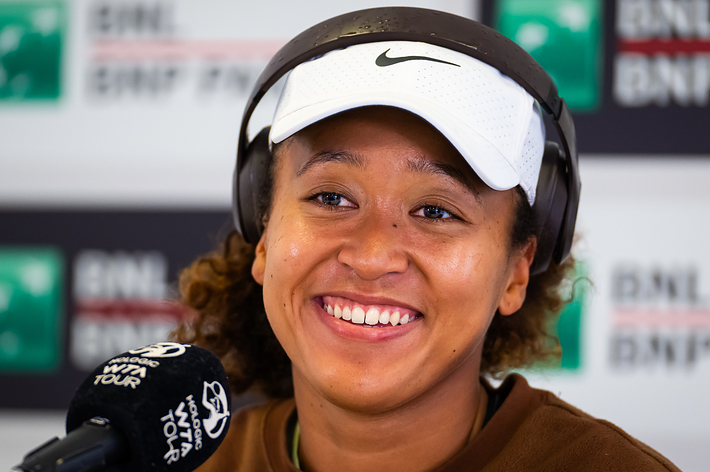 Naomi Osaka wearing a hat and smiling during a press conference