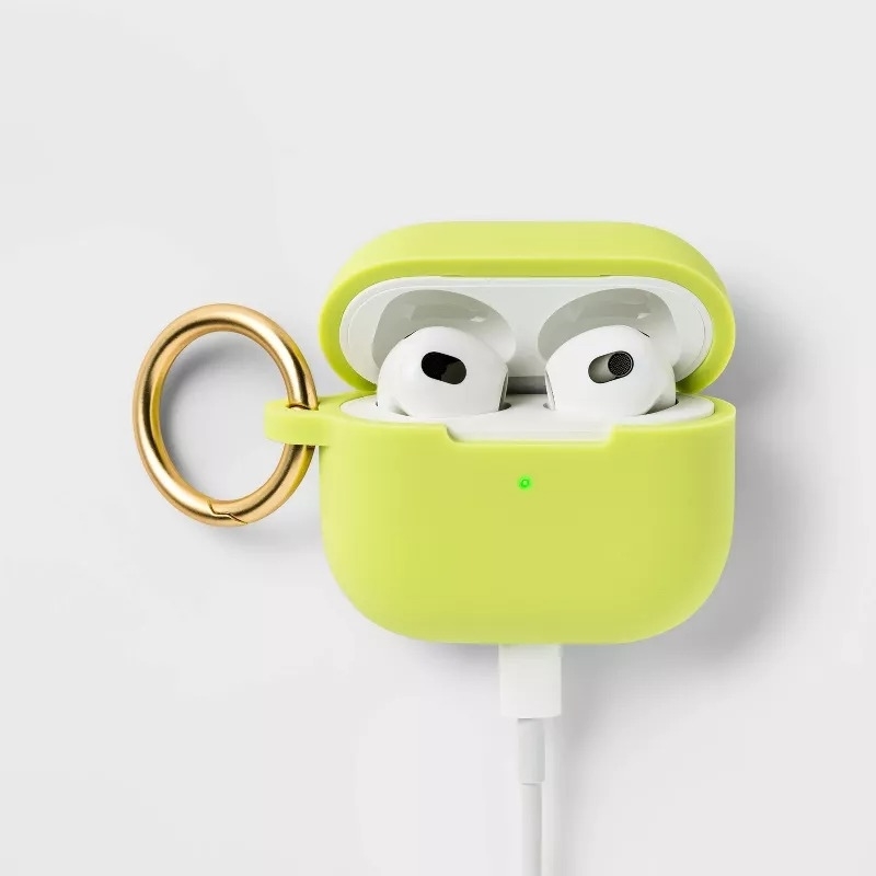 AirPods in a green charging case with keyring attached, plugged into a charging cable