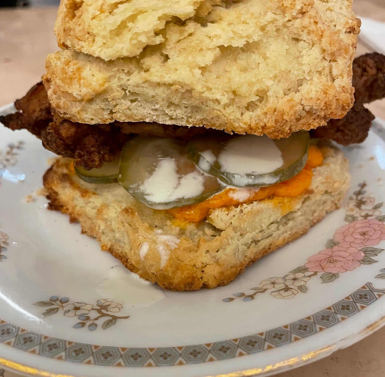 Fried chicken biscuit sandwich with pickles and sauce on a floral plate