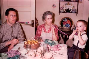 Family blowing party horns at a birthday party with cake on the table
