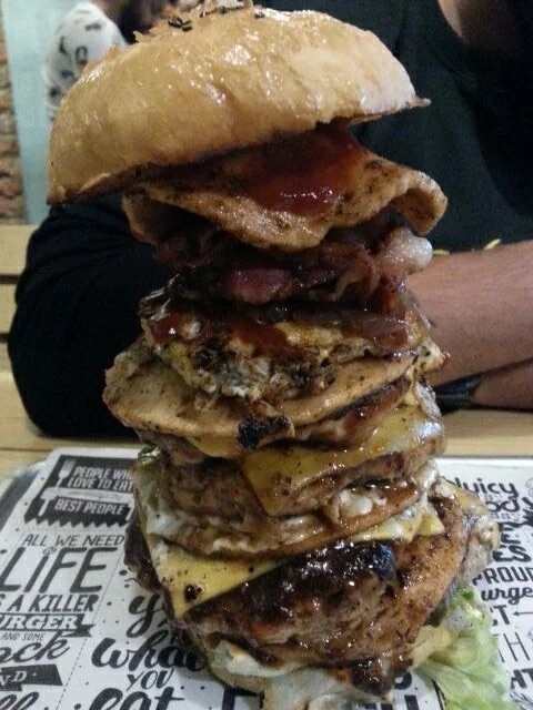 A towering burger with multiple beef patties, cheese slices, bacon, and sauce on a bun