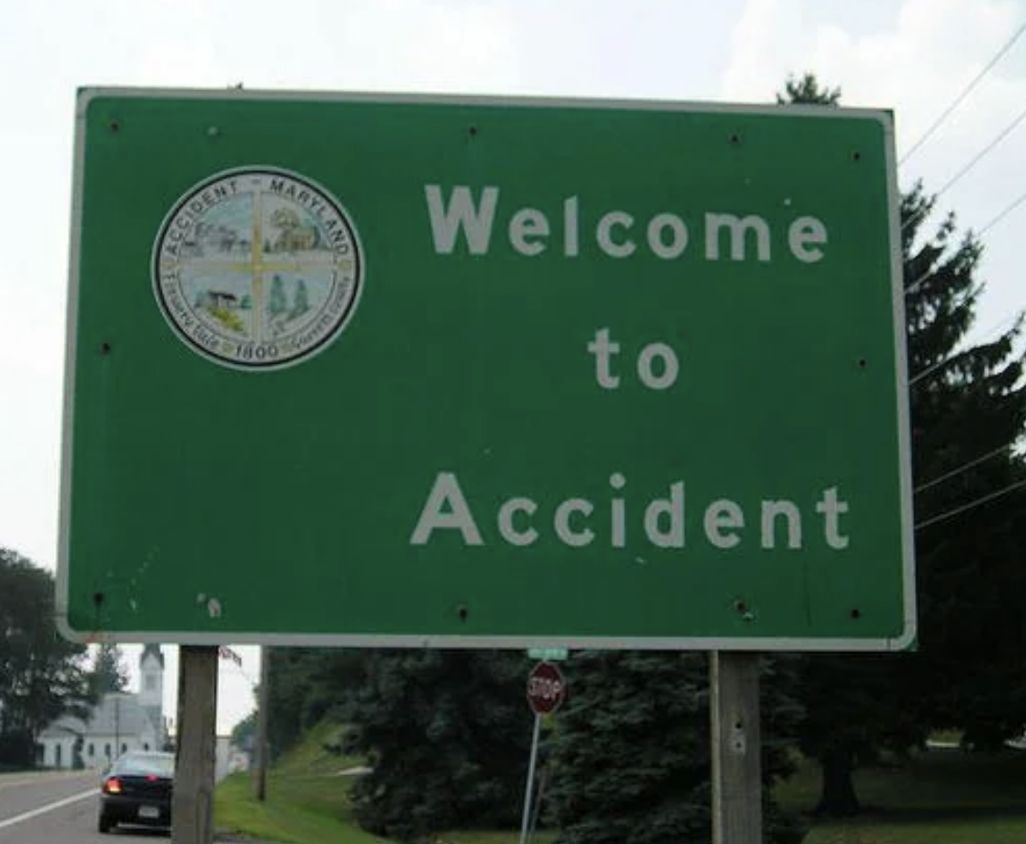 Welcome sign for the town called Accident with town seal, against a backdrop of a road and sky