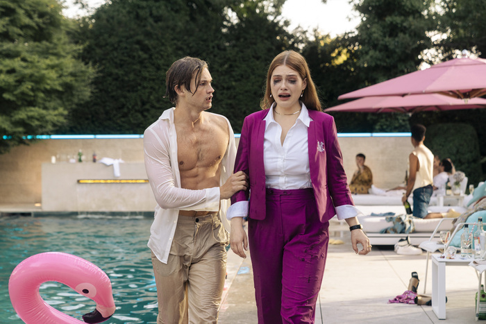 Personajes de película junto a piscina, hombre sin camisa y mujer con traje magenta, expresión preocupada