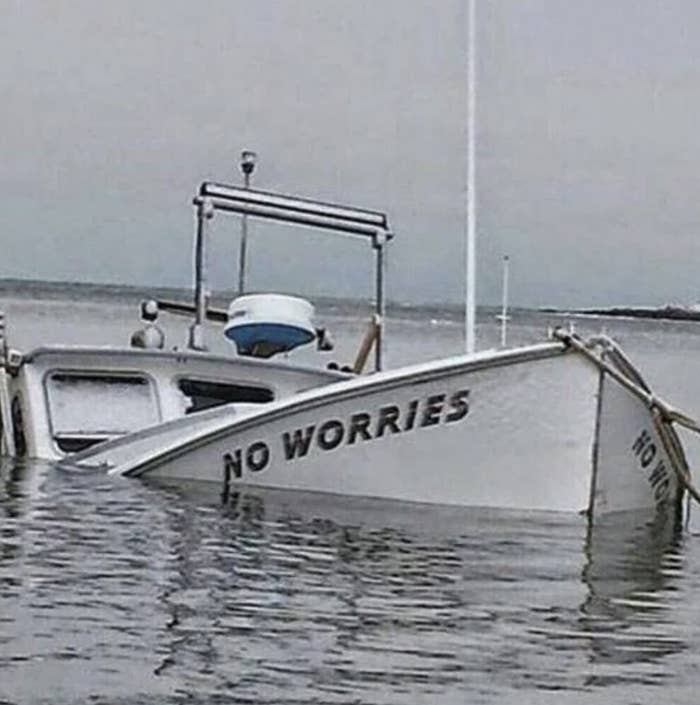 A partially submerged boat with the ironic name &quot;NO WORRIES&quot; visible on its side