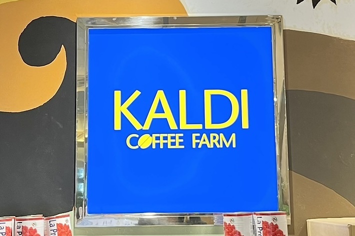 壁にカルディコーヒーファームのロゴがある店内、棚に商品が並んでいる。