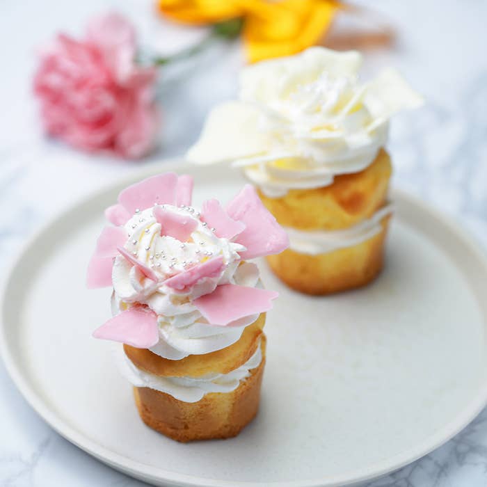 プレートの上には2つのカップケーキがあり、ピンクと白の花の形をしたトッピングが飾られています。