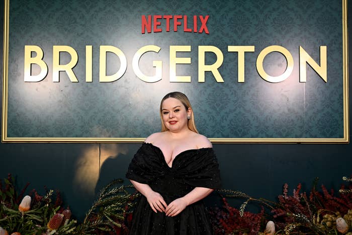 Nicola Coughlan stands in front of a "Bridgerton" sign, wearing an off-shoulder black gown