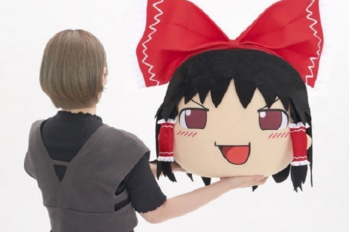 人物がアニメキャラクターの大きな頭部を持つぬいぐるみに触れている様子。